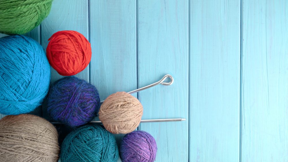Balls of yarn in different colors with knitting needles on a background of blue wood texture.